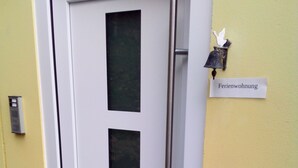 Ovi, jossa on huurrettu lasipaneeli, metallinen kahva ja viereisessä seinässä oleva kyltti, jossa lukee ”Ferienwohnung”.