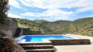 A swimming pool with stone steps and a view of a hilly landscape.