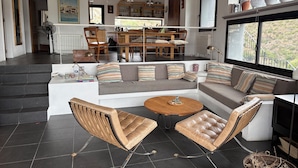 A spacious living area with a sofa, two leather chairs, a wooden coffee table, and a dining table with chairs.