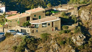 A hillside property with stone buildings, a garage, and parked cars.