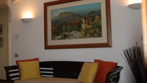 A room with a wooden floor, a black sofa with yellow and orange cushions, and a framed painting on the wall. - Beautiful Lucchese Apartment with Stunning Views (Lucca)