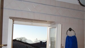 A bathroom with a window revealing a view of a building and mountains. - Beautiful Lucchese Apartment with Stunning Views (Lucca)