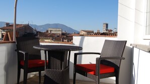 A balcony with wicker furniture and red cushions, overlooking a cityscape with buildings and a mountain in the distance. - Beautiful Lucchese Apartment with Stunning Views (Lucca)