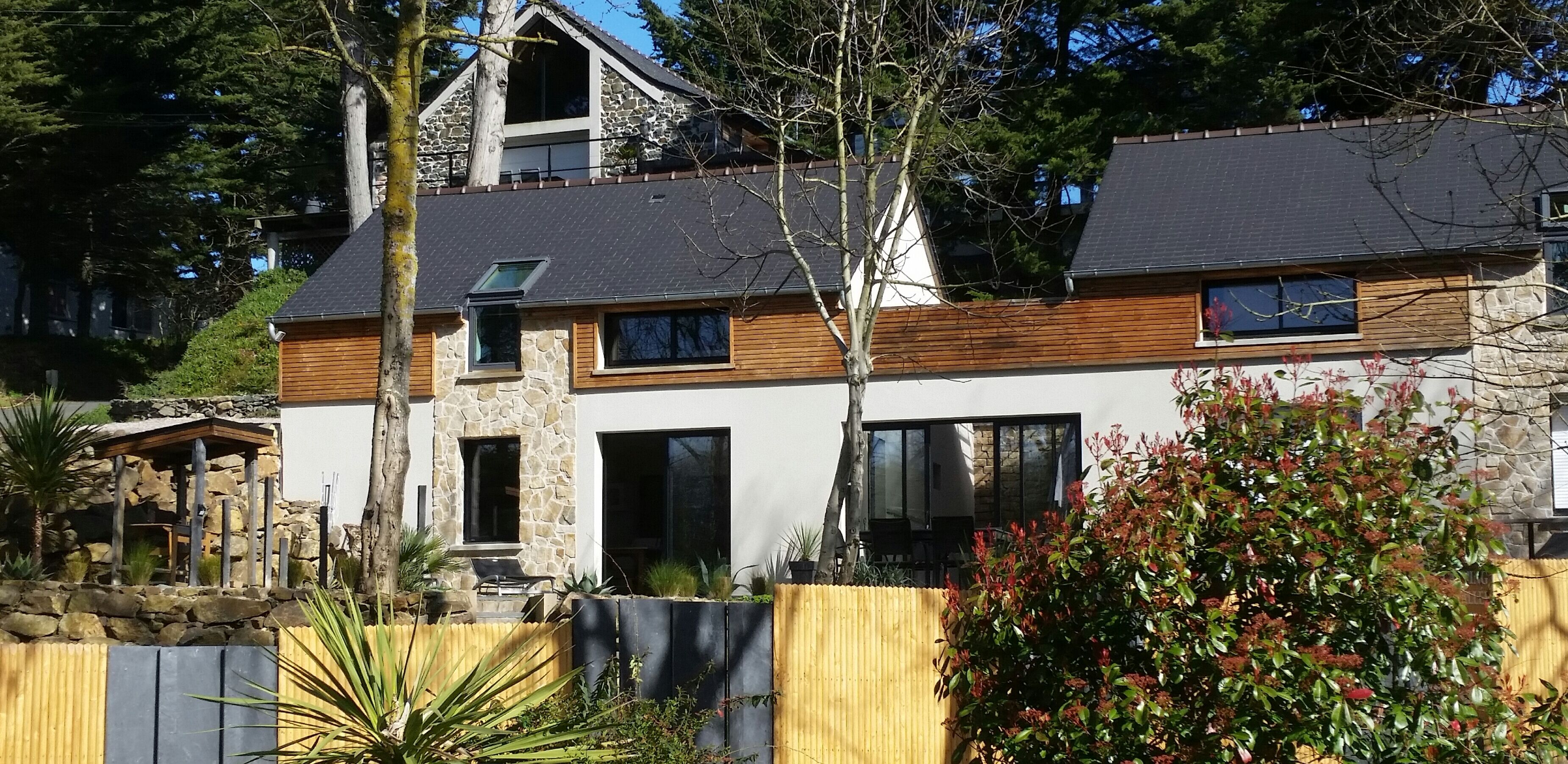 A modern two-story house with stone and wood exterior, large windows, and a well-maintained garden.