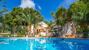 A swimming pool with a clear blue water surface, surrounded by palm trees and a white building with a balcony. - Apartment beach Sol de Mallorca 2 with pool (Cala Mesquida)