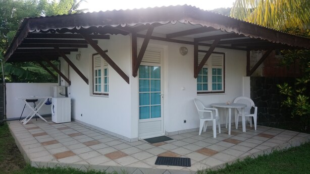A small, single-story building with a tiled patio, a covered outdoor seating area, and a washing machine.