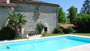 Une construction en pierre dotée d’une piscine, d’un patio avec des meubles d’extérieur et d’un jardin luxuriant.