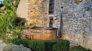 Un bâtiment en pierre doté d’un bain à remous en bois et d’une petite terrasse.