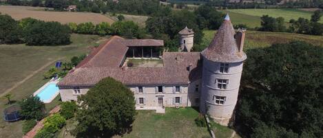 A large stone building with a tower, surrounded by fields and trees.