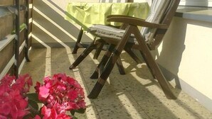 Un balcon avec deux chaises en bois, un coussin à rayures et une nappe verte.