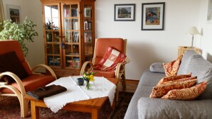Un salon comprenant un canapé, un fauteuil, un meuble en bois et une table sur laquelle est posé un vase de fleurs.