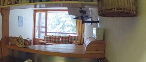 A compact kitchen with a built-in counter, wooden cabinets, and a window with a view of trees.