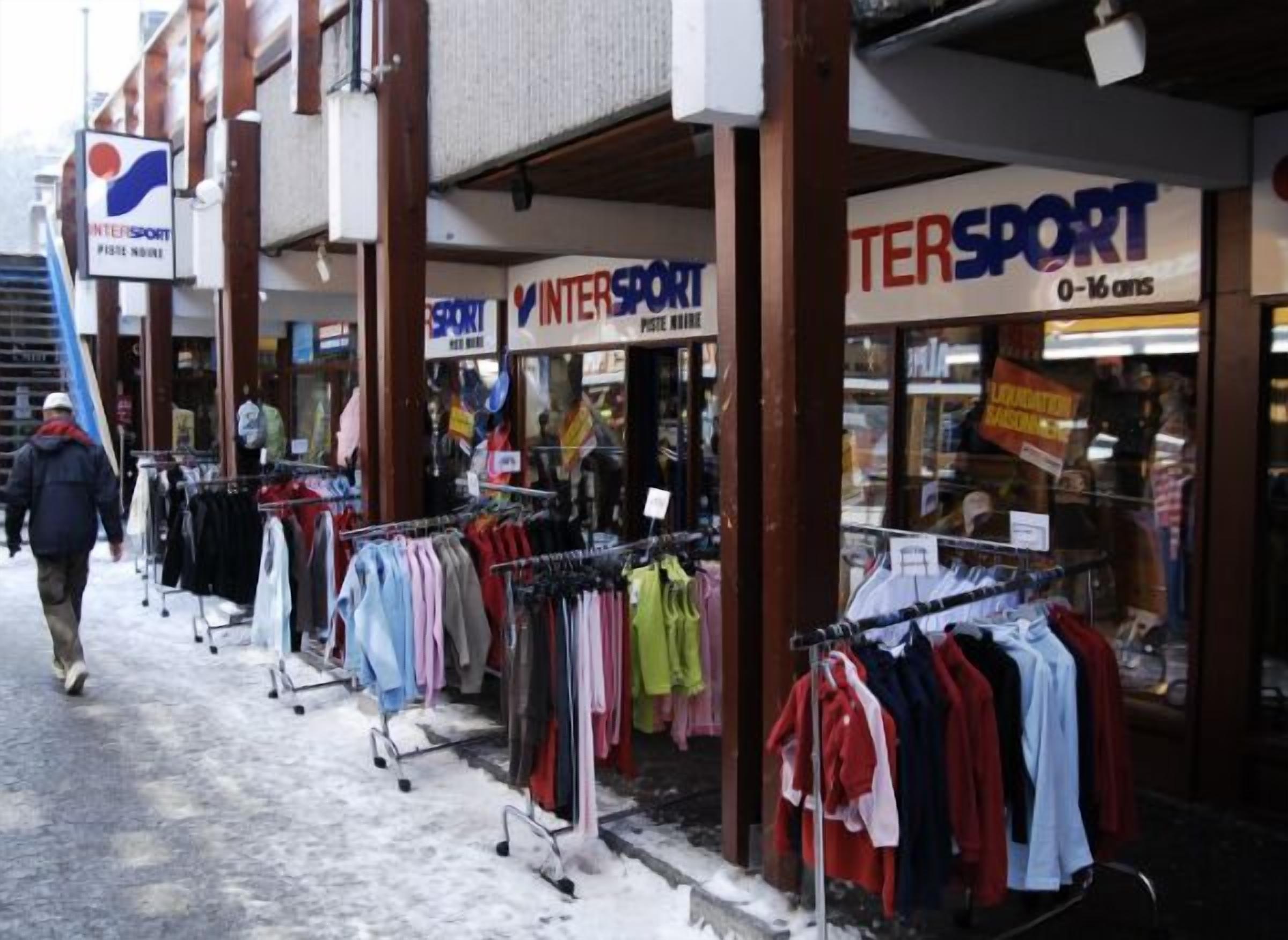 Un escaparate con varios puestos de ropa en el exterior, incluyendo un cartel de 'INTERSPORT' y 'TERSPORT 0-16'.