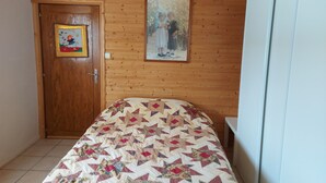A room with wooden walls, a bed with a patterned quilt, a door with a framed picture, and a painting on the wall. - Les Rousses-Bois d'avont (Bois-D'amont)