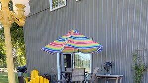 Eine Terrasse mit Gartenmöbeln, einem bunten Sonnenschirm und einem Garten mit Blumen und Steinen.