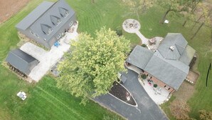 Vue aérienne d’une propriété résidentielle comprenant une grande maison, un garage plus petit attenant et une pelouse bien entretenue.