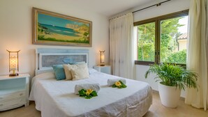 Een slaapkamer met een bed, twee nachtkastjes, een schilderij, een raam met gordijnen en een potplant.