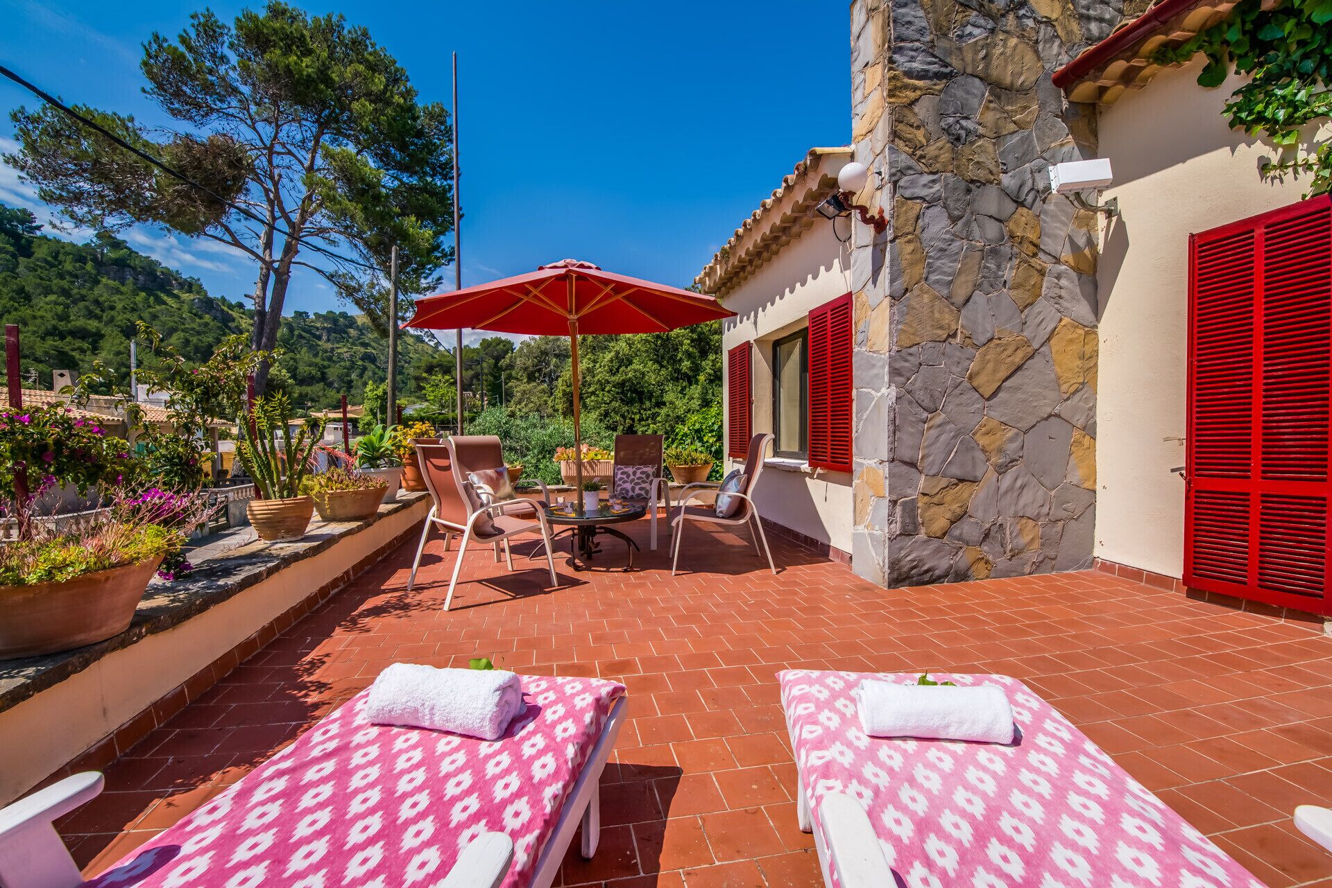 Une terrasse avec deux chaises longues, un parasol rouge et un mur en pierre.