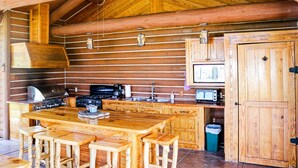 Een blokhut met houten inrichting, een keuken met fornuis, spoelbak en kastjes, en een eethoek met krukken.