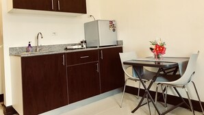 A compact kitchen with dark wood cabinets, a stainless steel refrigerator, a granite countertop, and a dining area with a table and two chairs. - Clean and cozy apartment (Cebu City)