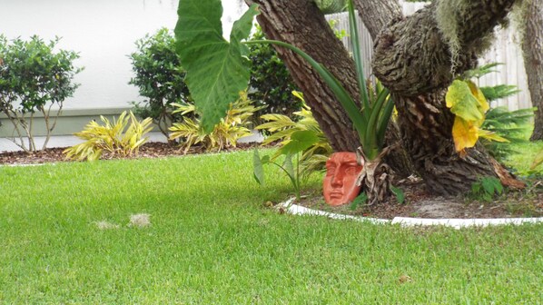Un jardín bien cuidado con diversas plantas, una máscara decorativa y el tronco de un árbol.
