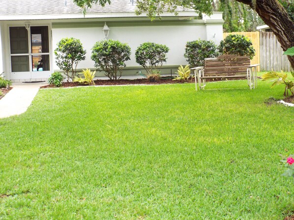 A well-maintained lawn with a wooden bench and a small garden area with various plants. - TWO BEDROOM HEATED POOL HOME - FREE CABLE AND WI-FI (Spring Hill)