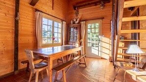 Een houten cabin interieur met een houten eettafel, bankjes en een raam met gordijnen.
