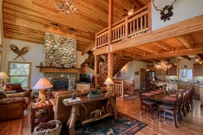 A spacious living area with a stone fireplace, wooden ceiling, and a dining table set for six.