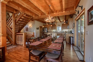 A wooden interior with a dining table set for six, a staircase, and a kitchen area.