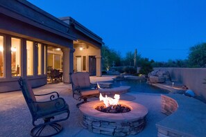 Une terrasse avec un foyer en pierre, du mobilier d’extérieur et une piscine.