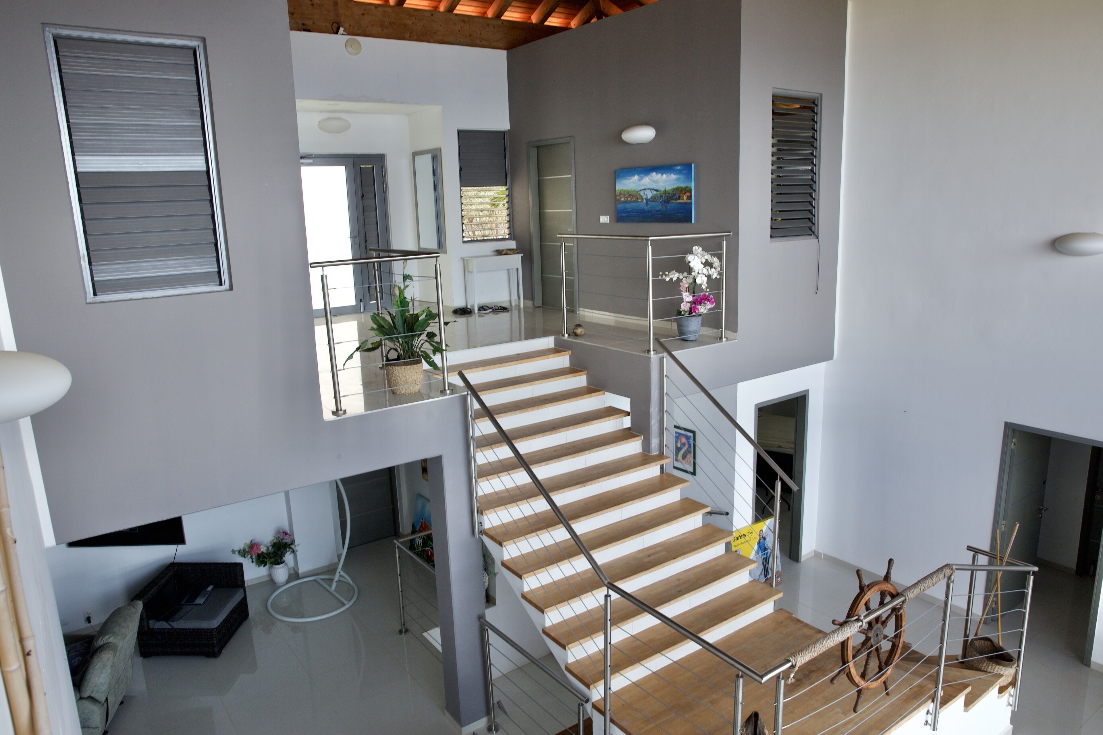Un intérieur à plusieurs niveaux, avec un escalier, une plante en pot et un tableau accroché au mur.