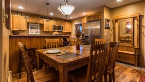 Une cuisine avec des meubles de rangement en bois, une table à manger pour quatre personnes et un réfrigérateur.