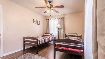 Une chambre avec deux lits simples, un ventilateur de plafond, une fenêtre avec des rideaux et un tapis à motifs.