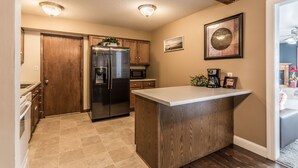 A compact kitchen with wooden cabinets, a stainless steel refrigerator, a microwave, and a small island counter. - Relaxing and spacious single family in heart of Overland Park (Overland Park)
