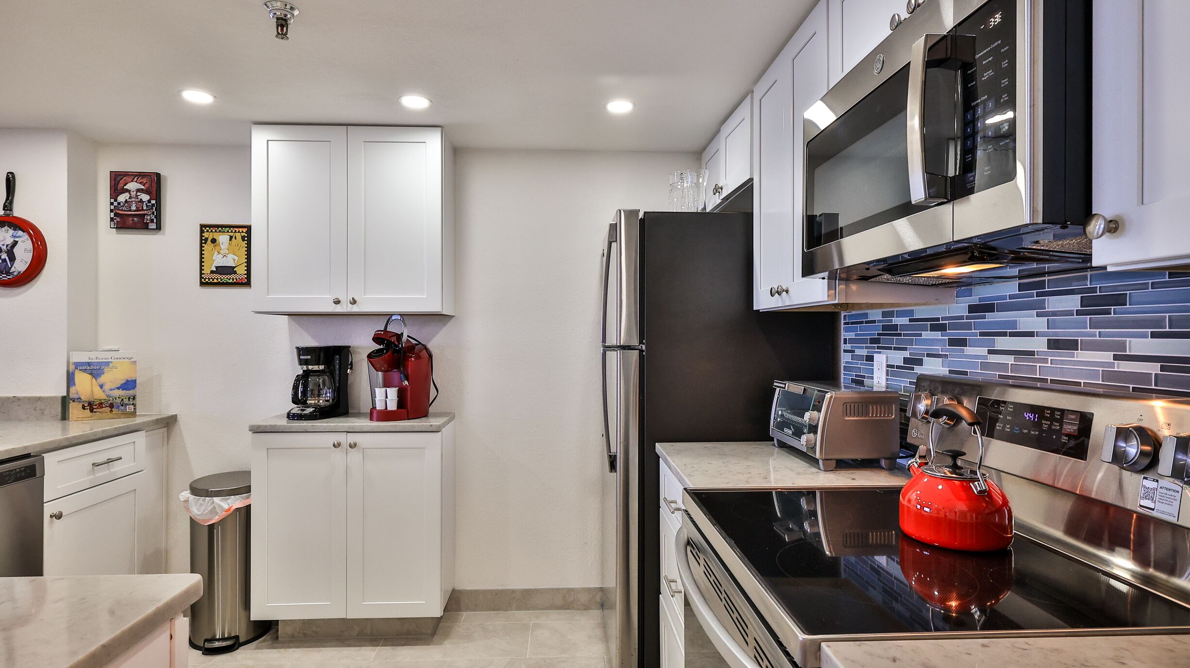 A modern kitchen with white cabinets, a stainless steel refrigerator, a microwave, and a red kettle.
