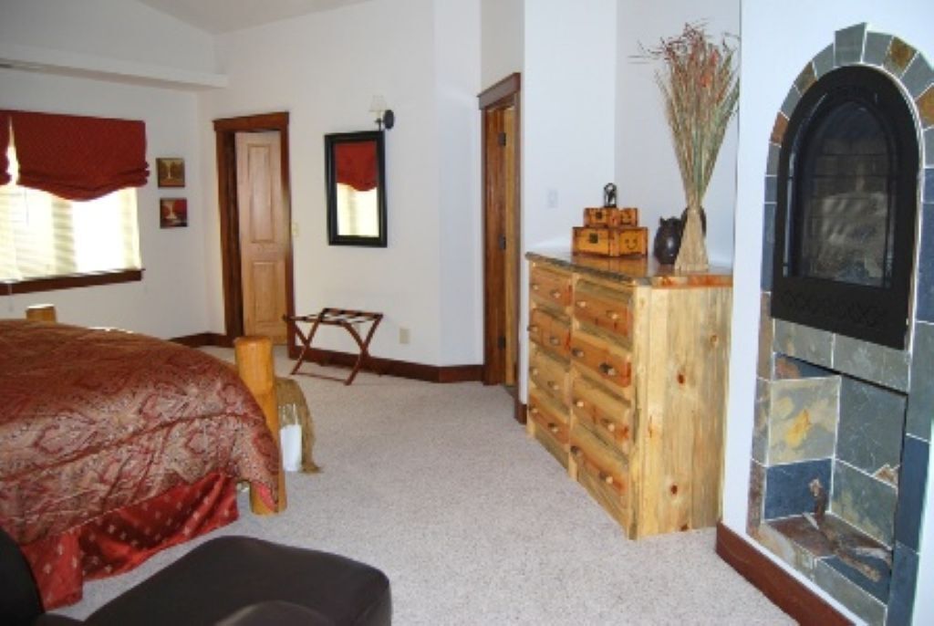 A bedroom with a bed, a dresser, a mirror, and a fireplace.