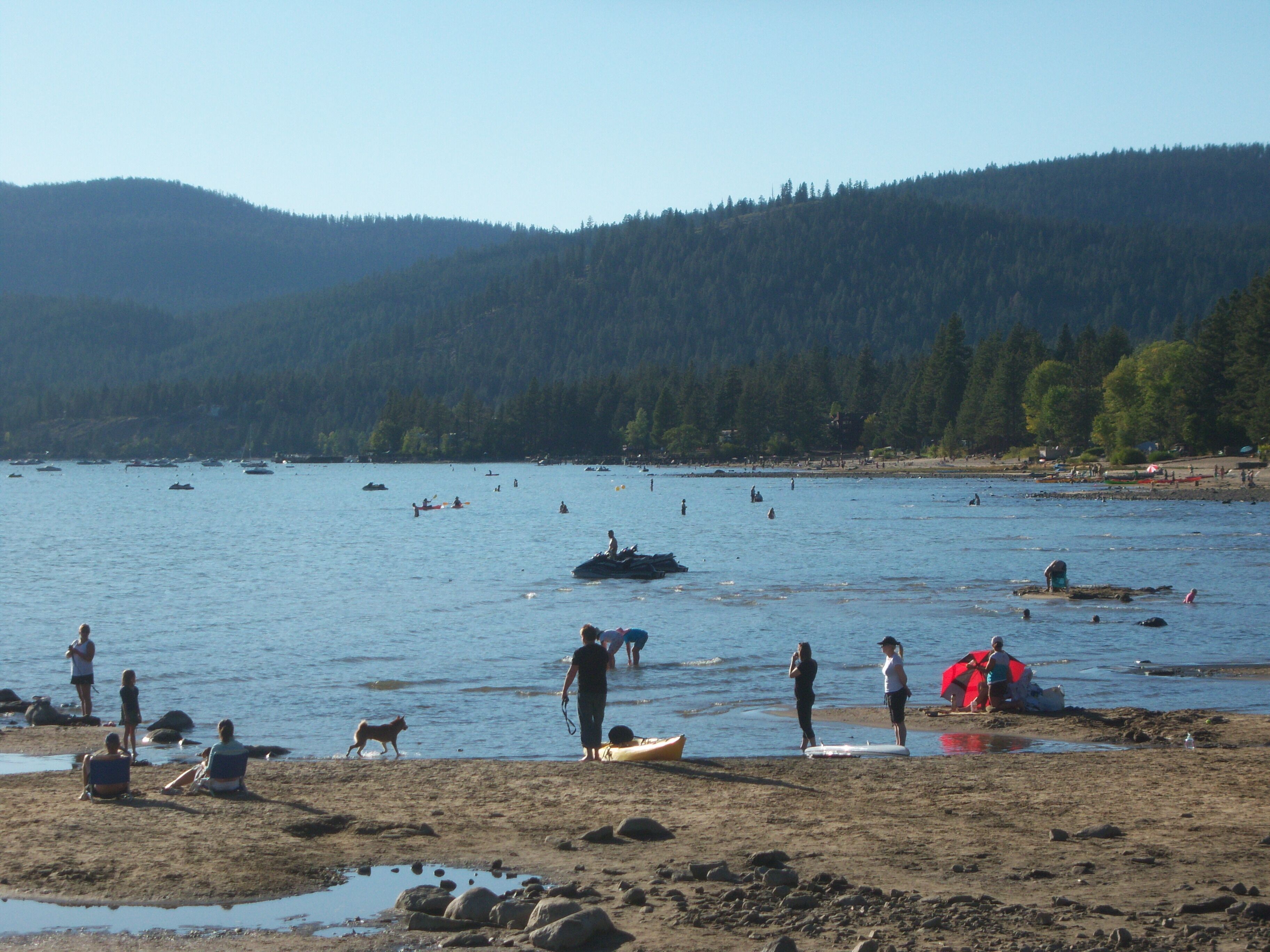A beach with people, boats, and a forested hill in the background.