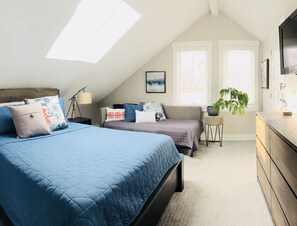 Une chambre avec deux lits, un canapé, une commode, une lampe et une fenêtre avec des stores.