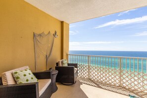 Een balkon met rieten meubels, een wit gesneden hekwerk en uitzicht op de oceaan.