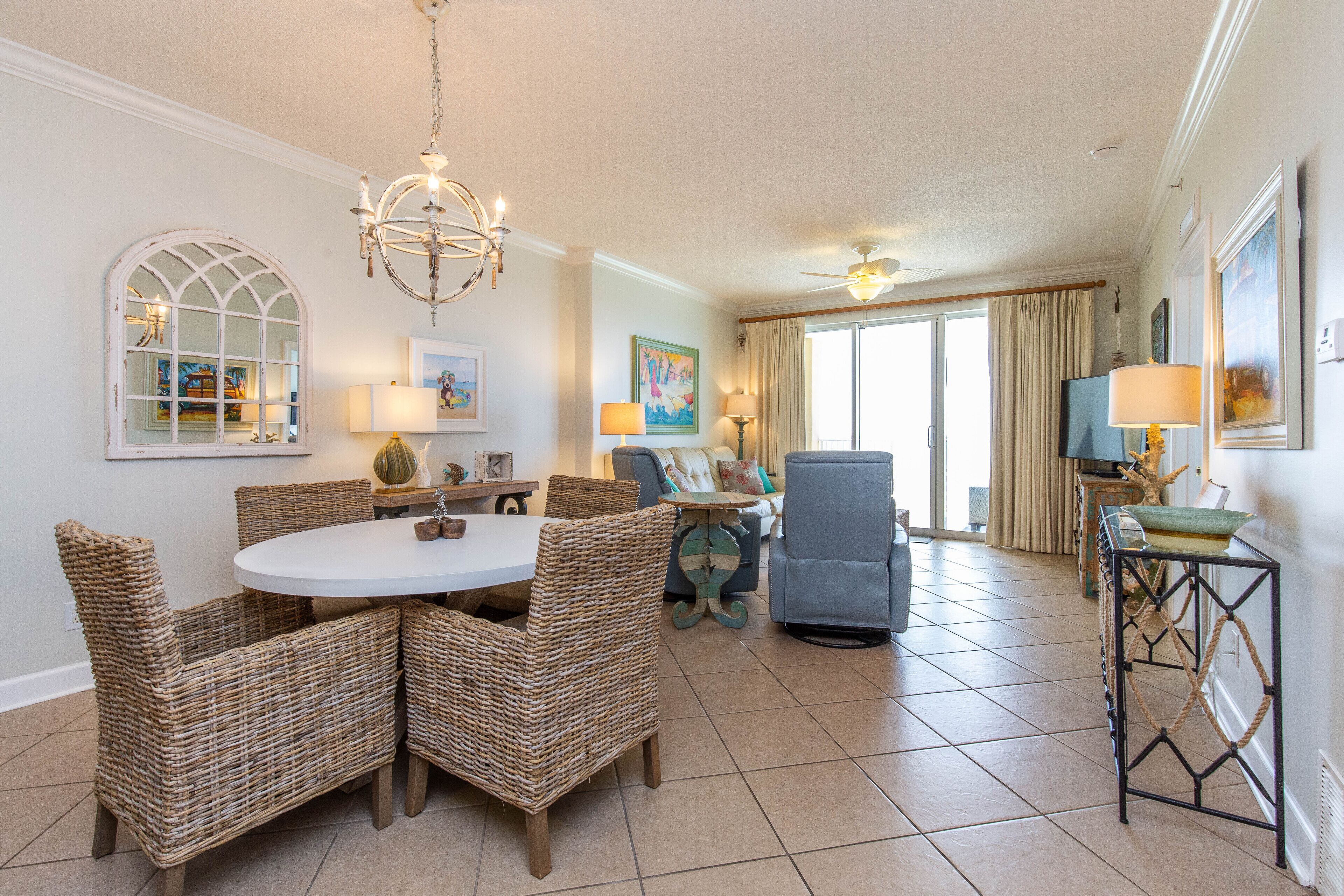 A spacious living room with a round dining table, wicker chairs, a blue sofa, and a ceiling fan.