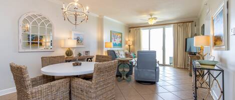 A spacious living room with a round dining table, wicker chairs, a blue sofa, and a ceiling fan.