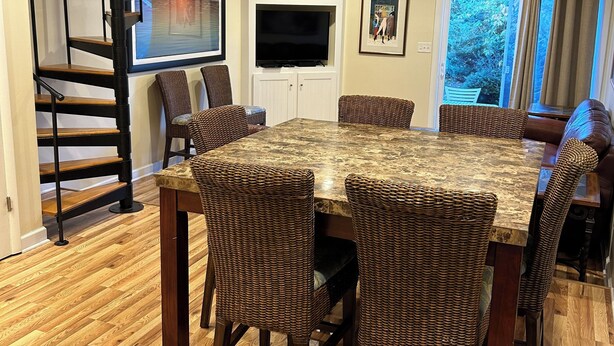 Un coin repas avec une grande table en bois et des chaises en osier, un téléviseur encastré et un escalier.