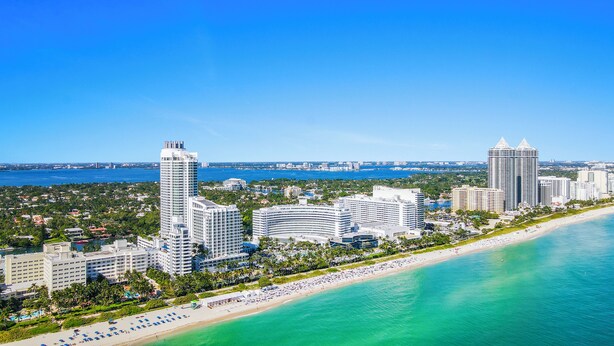 A coastal cityscape with high-rise hotels, a beach, and a clear blue sky.