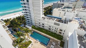 A high-rise hotel with a rooftop pool, beach view, and palm trees.