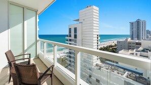 A balcony with wicker chairs, a view of the ocean, and modern buildings.