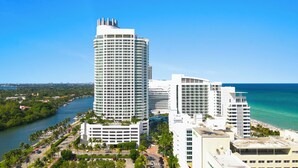 A high-rise hotel with multiple floors, a waterfront view, and a parking area with palm trees.
