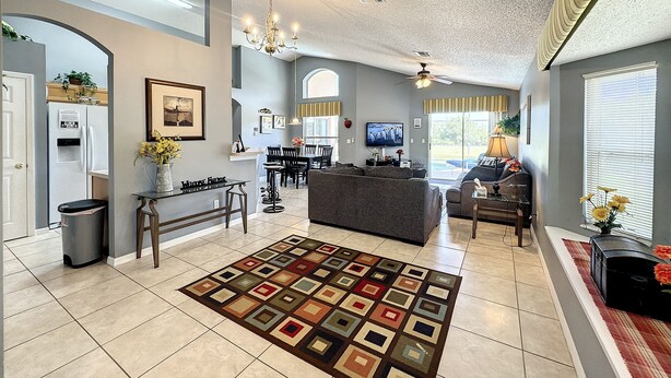 A spacious living room with a large sofa, a coffee table, and a TV. There is a dining area with a table and chairs, and a kitchen area with a refrigerator and sink. - Resort Community - Waterfront Home Next Door to Disney!  (Kissimmee)