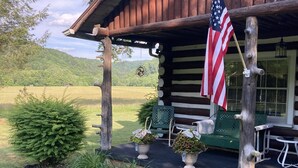 A rustic cabin with a porch, an American flag, and potted plants.