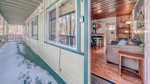 A covered porch with a wooden ceiling, a green-framed window, and a wooden door leading to a living room with a couch and a table. - RECHARGE,  Pets Welcome,  Fast Wifi,  Opt HOT TUB (Ruidoso)