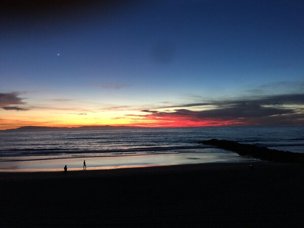 A beach at sunset with a person walking on the sand.